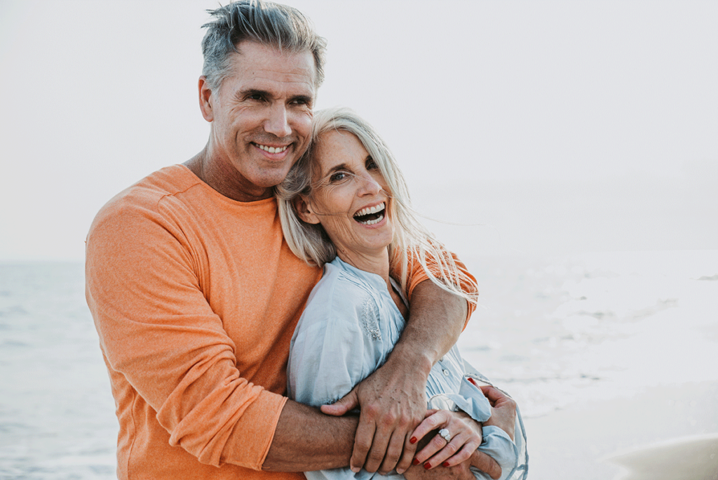 middle aged couple with beautiful smiles embracing on the beach