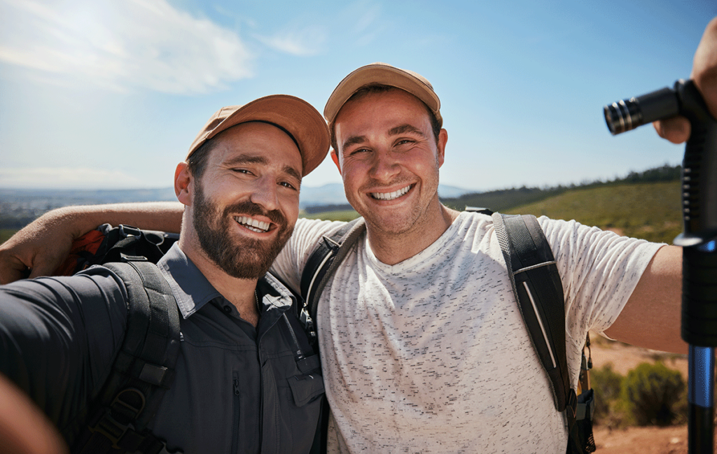 two young men out hiking in the country smile for the camera displaying perfectly health teeth and gums