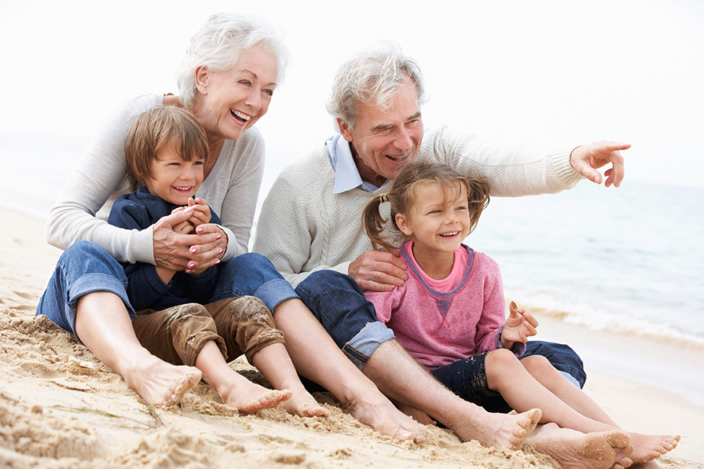 older couple playing with their two grandchildren on the beach and all four are displaying brilliant smiles